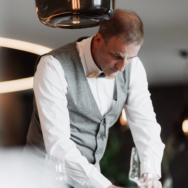 Erfüllender Urlaub in Ihrem Luxus-Chalet in Südtirol Mann in Weste und Fliege deckt Tisch mit Gläsern