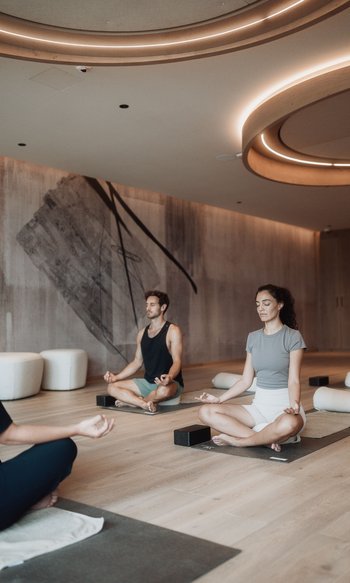 Your hotels in South Tyrol: the home of abundance People meditating cross-legged on yoga mats in a modern fitness room