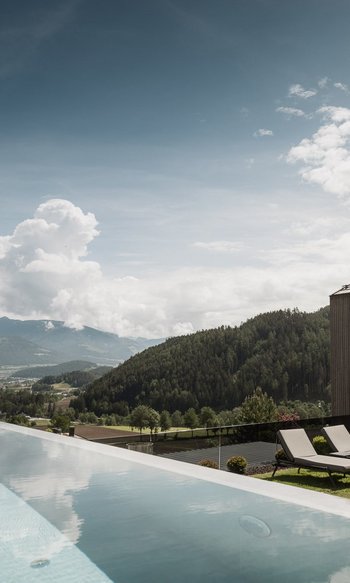 Erfüllender Urlaub in Ihrem Luxus-Chalet in Südtirol Infinity-Pool mit Bergblick und modernem Holzhaus bei sonnigem Himmel
