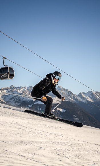 Your hotels in South Tyrol: the home of abundance Skier on slope with cable car and snow-covered mountains in the background