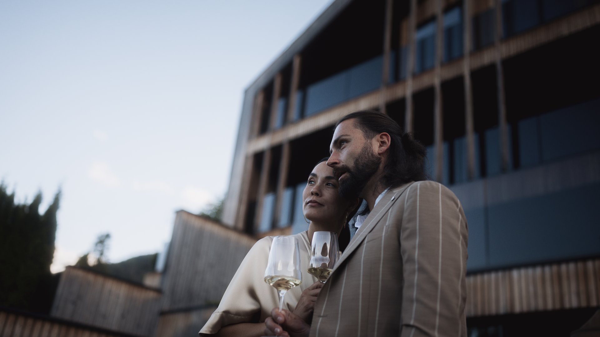 Your hotels in South Tyrol: the home of abundance Couple holding wine glasses by modern building at sunset