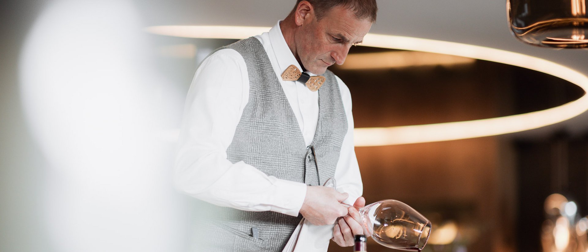 Erfüllender Urlaub in Ihrem Luxus-Chalet in Südtirol Mann in Weste und Fliege gießt Wein in ein Glas in elegantem Restaurant