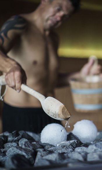 Erfüllender Urlaub in Ihrem Luxus-Chalet in Südtirol Mann gießt Wasser auf heiße Steine in der Sauna