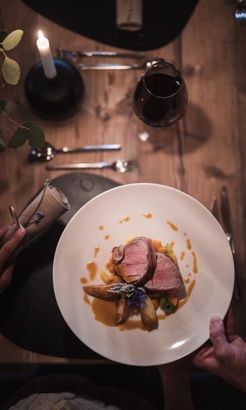 Your hotels in South Tyrol: the home of abundance Set table with candle, wine glass, and plated meat dish on white plate
