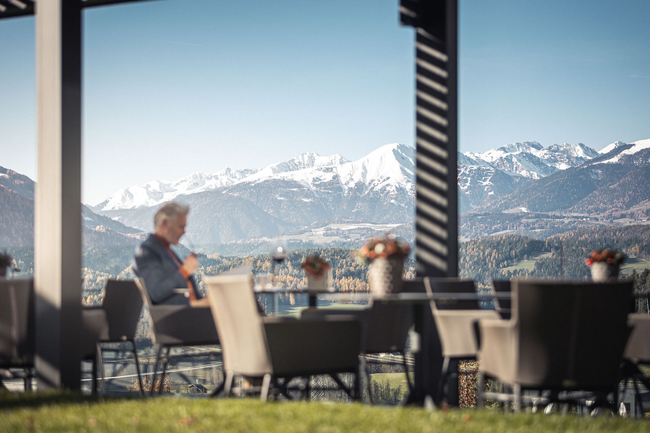 Die Quelle der Erfüllung: Ihr Hotel am Kronplatz Mann sitzt draußen mit Bergblick und trinkt Kaffee auf Terrasse
