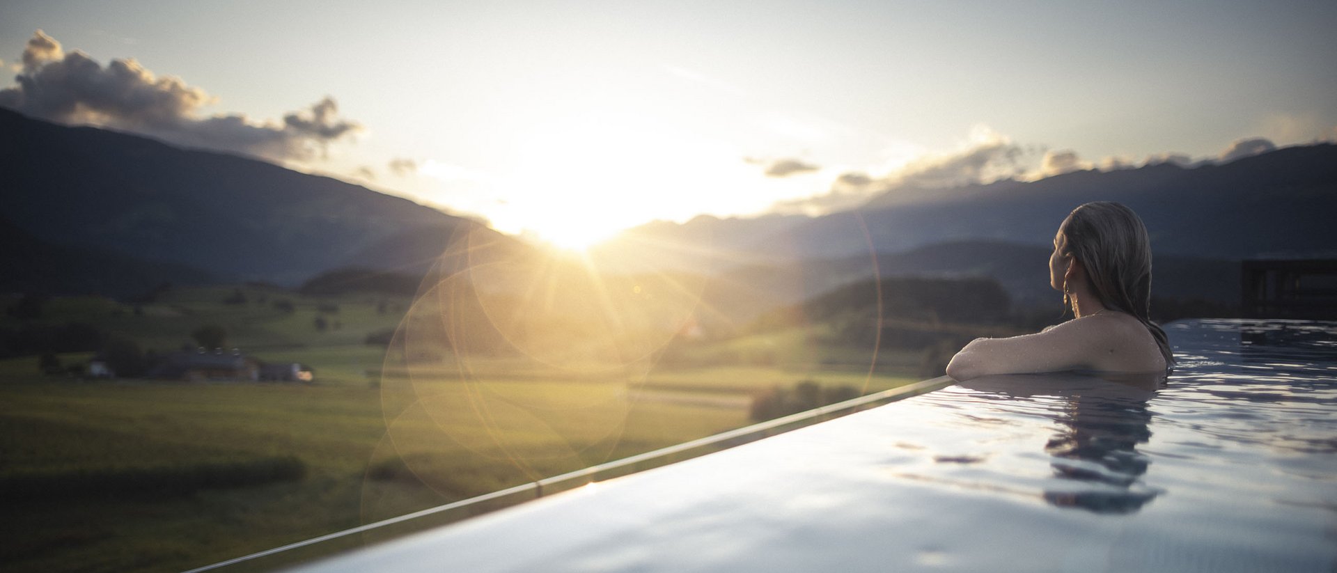 Die Quelle der Erfüllung: Ihr Hotel am Kronplatz Frau entspannt im Infinity-Pool bei Sonnenuntergang mit Bergblick