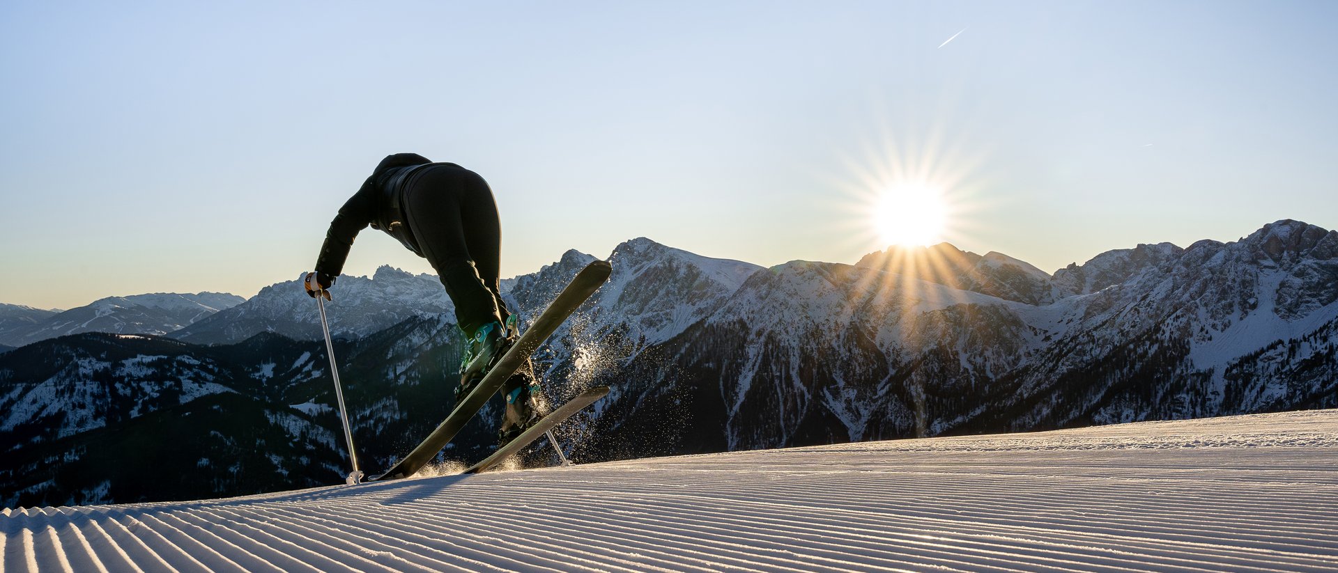 Die Quelle der Erfüllung: Ihr Hotel am Kronplatz Skifahrer springt über frisch präparierte Piste bei Sonnenuntergang in den Bergen