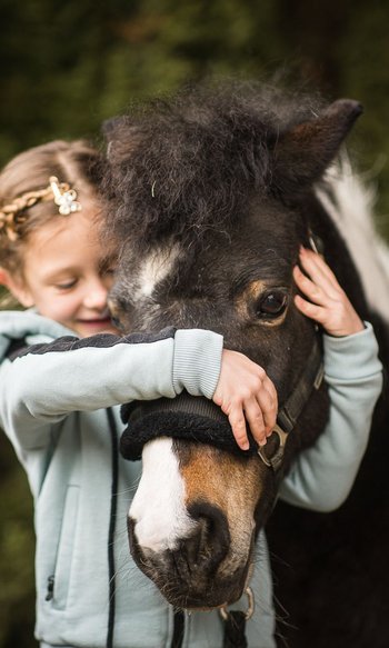 Your hotels in South Tyrol: the home of abundance Girl hugging and holding a black pony with a white mark