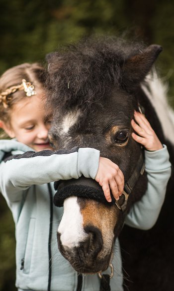 Your hotels in South Tyrol: the home of abundance Girl hugging and holding a black pony with a white mark