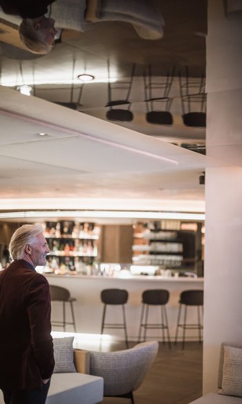 Your hotels in South Tyrol: the home of abundance Older man standing in stylish bar with stools and shelves in the background