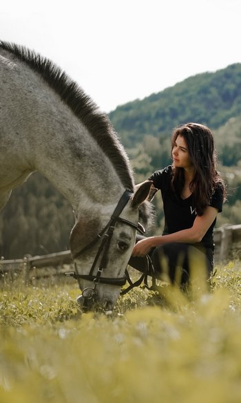 Your hotels in South Tyrol: the home of abundance Woman kneeling beside a grazing horse in a meadow with mountains behind