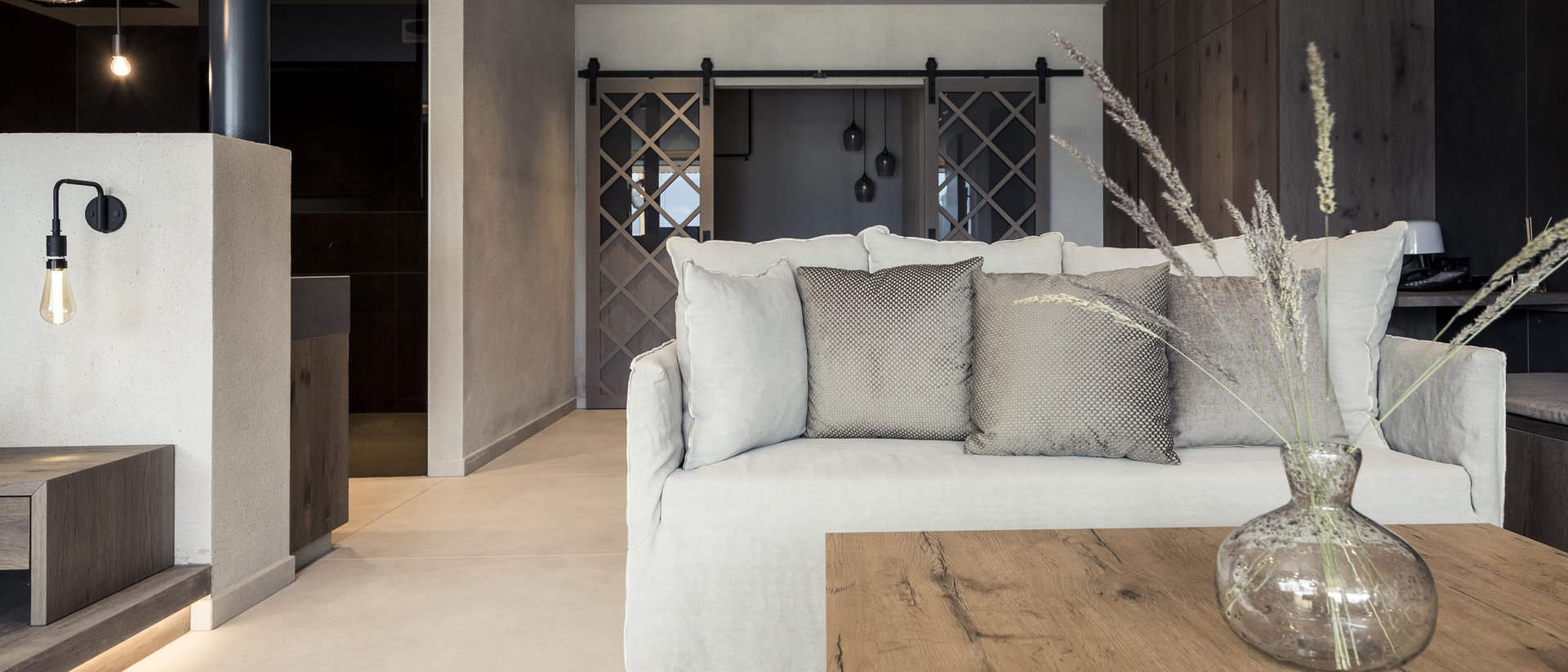 Erfüllender Urlaub in Ihrem Luxus-Chalet in Südtirol Moderner Wohnbereich mit hellgrauem Sofa, Holz-Tisch und Deko-Vase