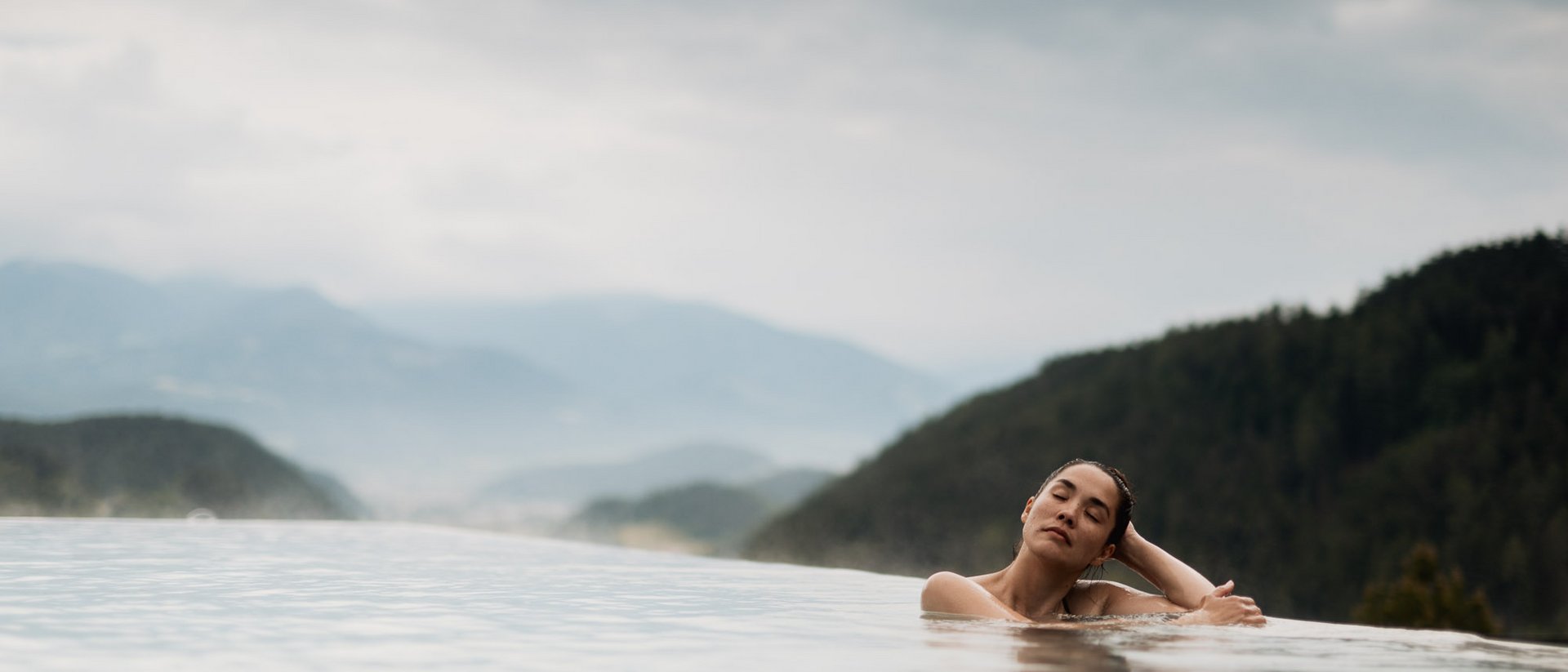 Erfüllender Urlaub in Ihrem Luxus-Chalet in Südtirol Frau entspannt in Infinity-Pool mit Bergblick und bewölktem Himmel