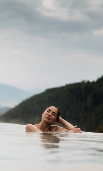 Your hotels in South Tyrol: the home of abundance Woman relaxing in infinity pool with mountain views and cloudy sky