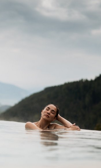 Your hotels in South Tyrol: the home of abundance Woman relaxing in infinity pool with mountain views and cloudy sky