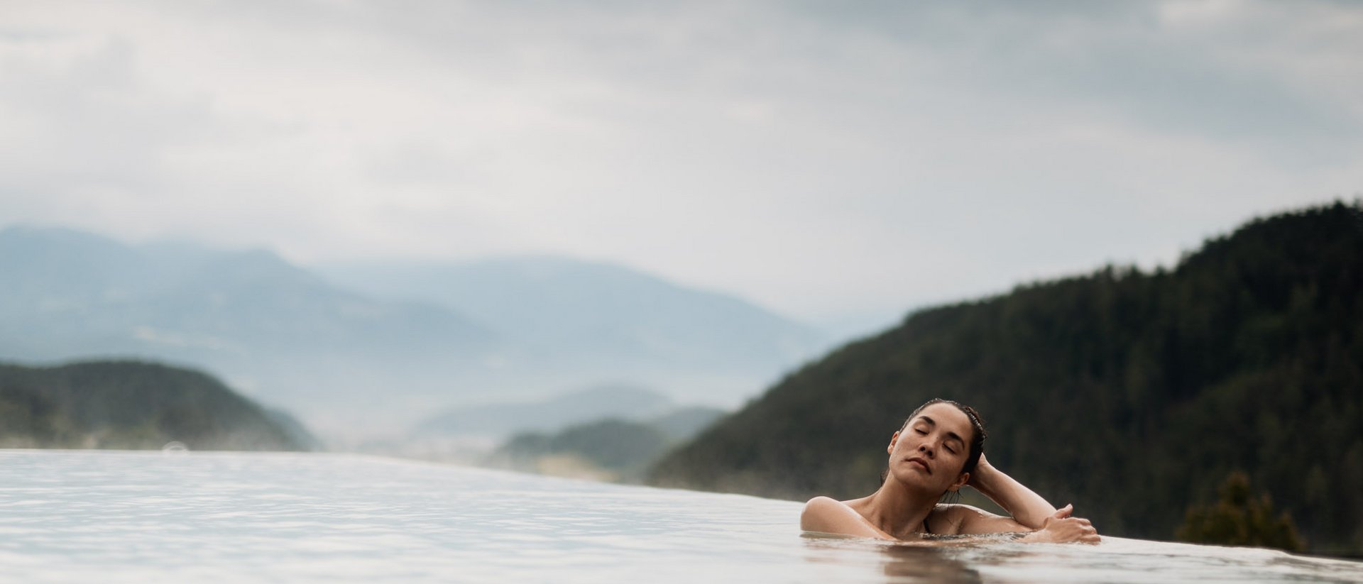 Erfüllender Urlaub in Ihrem Luxus-Chalet in Südtirol Frau entspannt in Infinity-Pool mit Bergblick und bewölktem Himmel