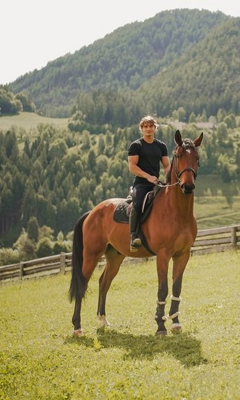 Your hotels in South Tyrol: the home of abundance Man riding a brown horse on a meadow with mountains in the background