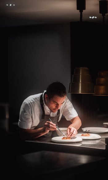 Your hotels in South Tyrol: the home of abundance Chef carefully plating gourmet dishes in dimly lit restaurant kitchen
