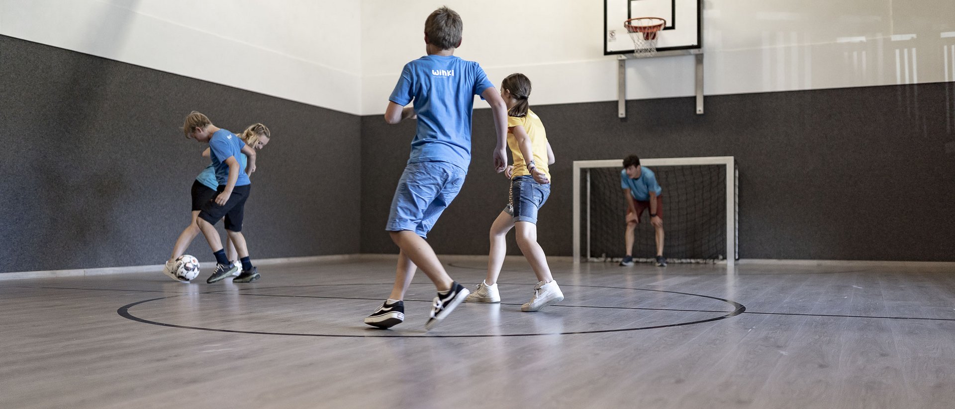 Die Quelle der Erfüllung: Ihr Hotel am Kronplatz Kinder spielen Fußball in einer Indoor-Sporthalle mit Basketballkorb und Tor
