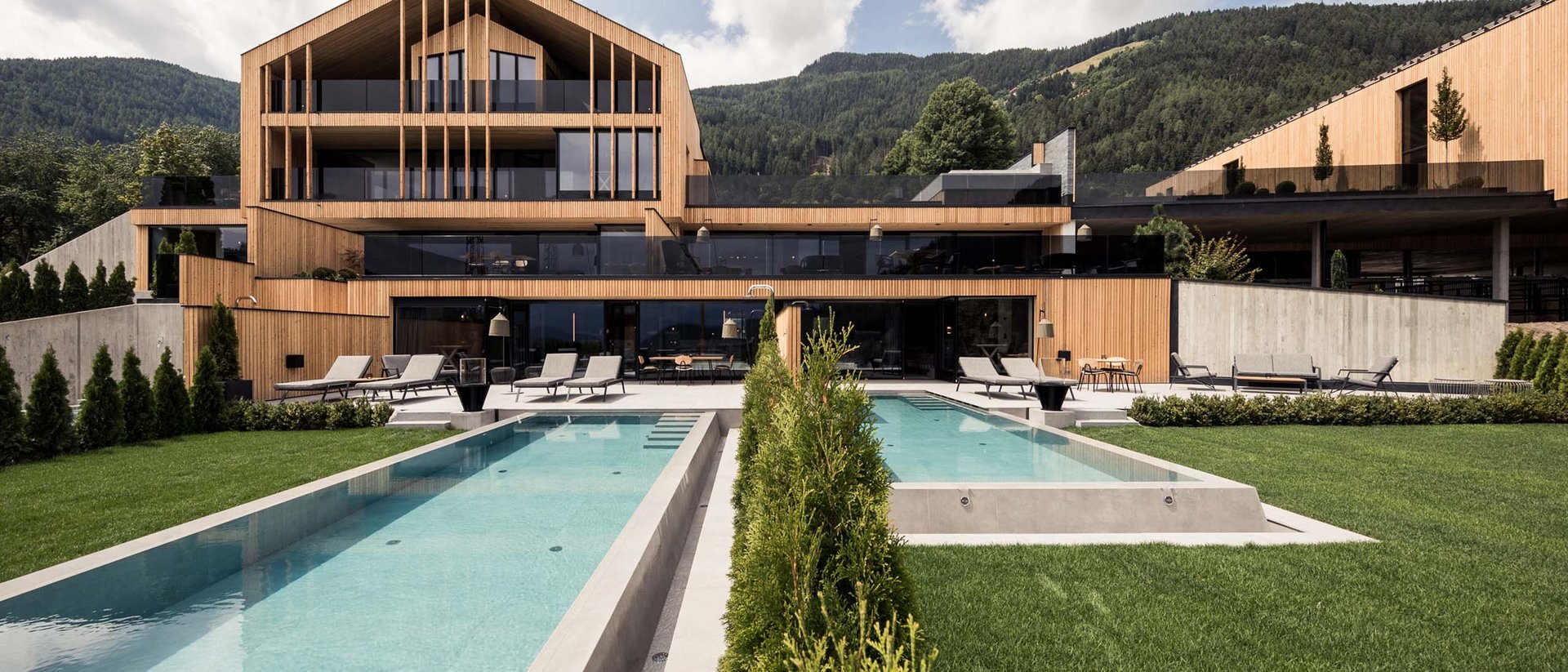 Erfüllender Urlaub in Ihrem Luxus-Chalet in Südtirol Modernes Holzhaus mit Pool und Liegestühlen vor Wald und Bergen