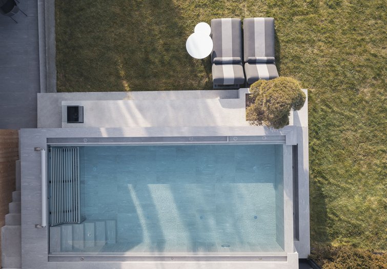 Die Quelle der Erfüllung: Ihr Hotel am Kronplatz Vogelperspektive eines modernen Pools mit zwei Liegestühlen und einem Tisch im Garten