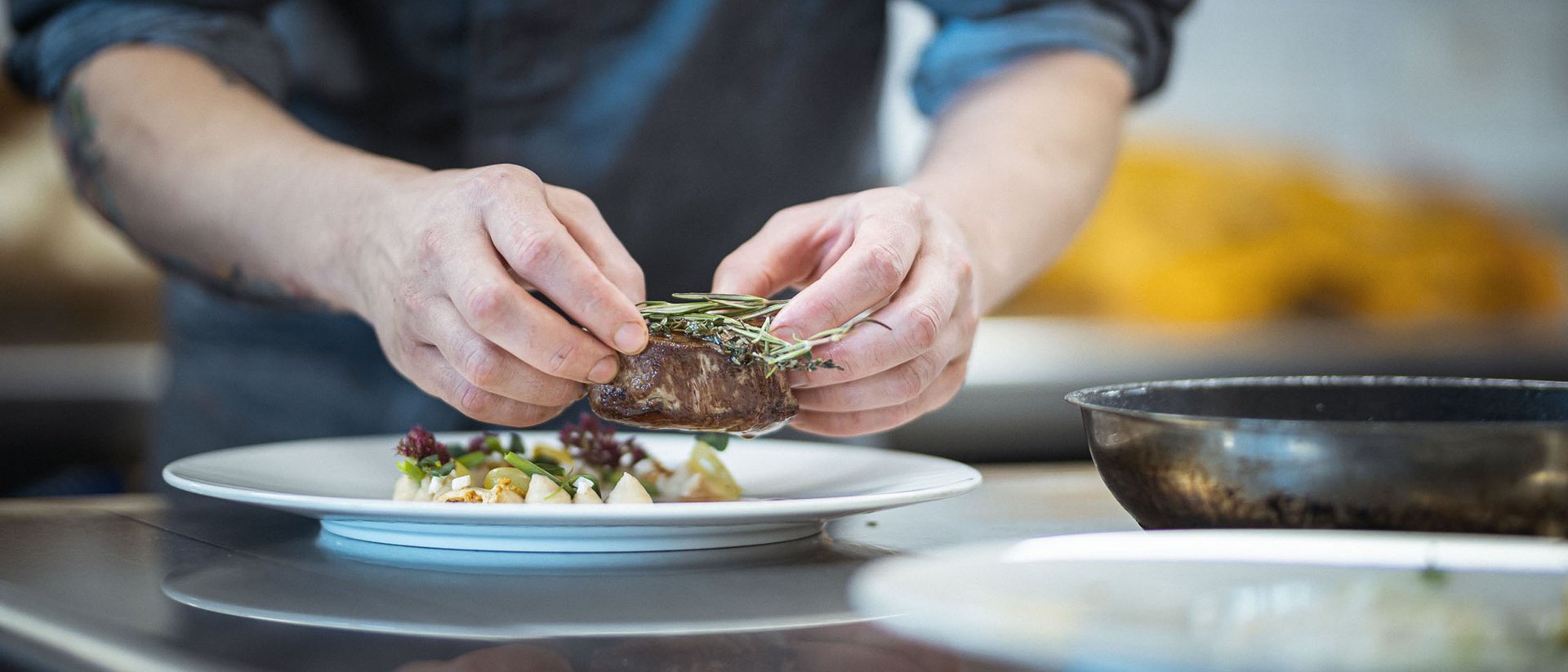 Die Quelle der Erfüllung: Ihr Hotel am Kronplatz Koch richtet zartes Steak auf einem Teller mit frischen Kräutern an