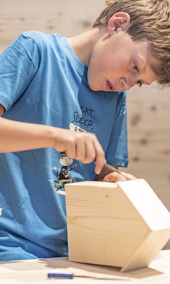 Your hotels in South Tyrol: the home of abundance Boy focused on carving a wooden object in workshop