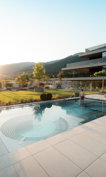 Your hotels in South Tyrol: the home of abundance Man entering modern outdoor pool at sunset in luxury resort