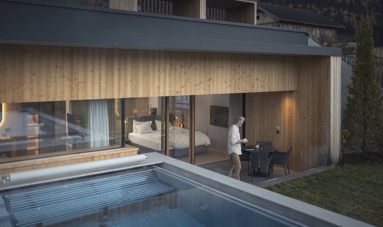 Die Quelle der Erfüllung: Ihr Hotel am Kronplatz Mann auf Terrasse vor modernem Holzhaus mit Swimmingpool