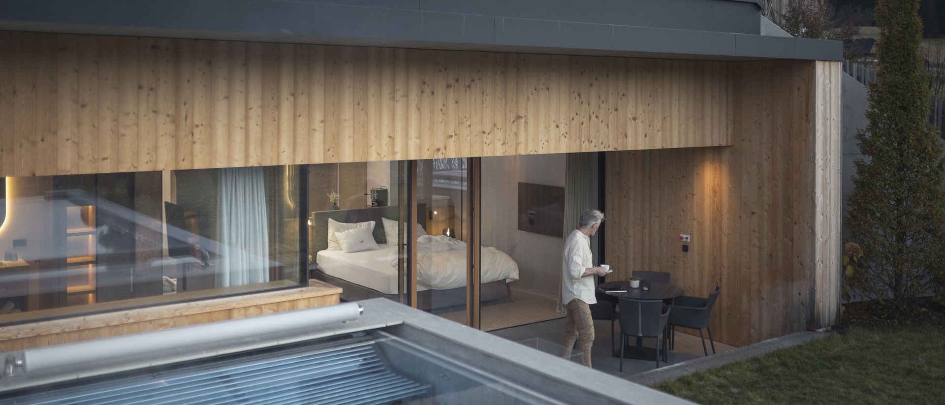 Die Quelle der Erfüllung: Ihr Hotel am Kronplatz Mann auf Terrasse vor modernem Holzhaus mit Swimmingpool