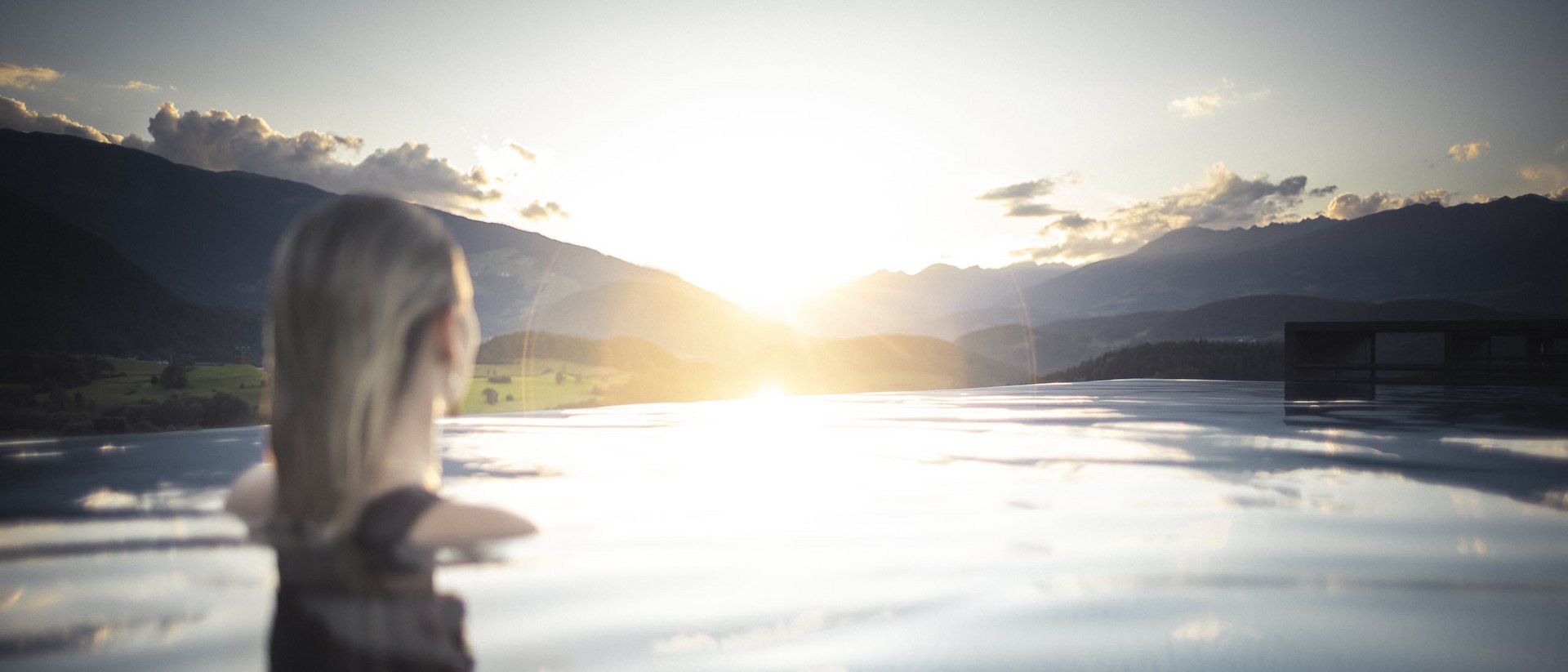 Die Quelle der Erfüllung: Ihr Hotel am Kronplatz Frau im Pool mit Blick auf Sonnenuntergang und Berge