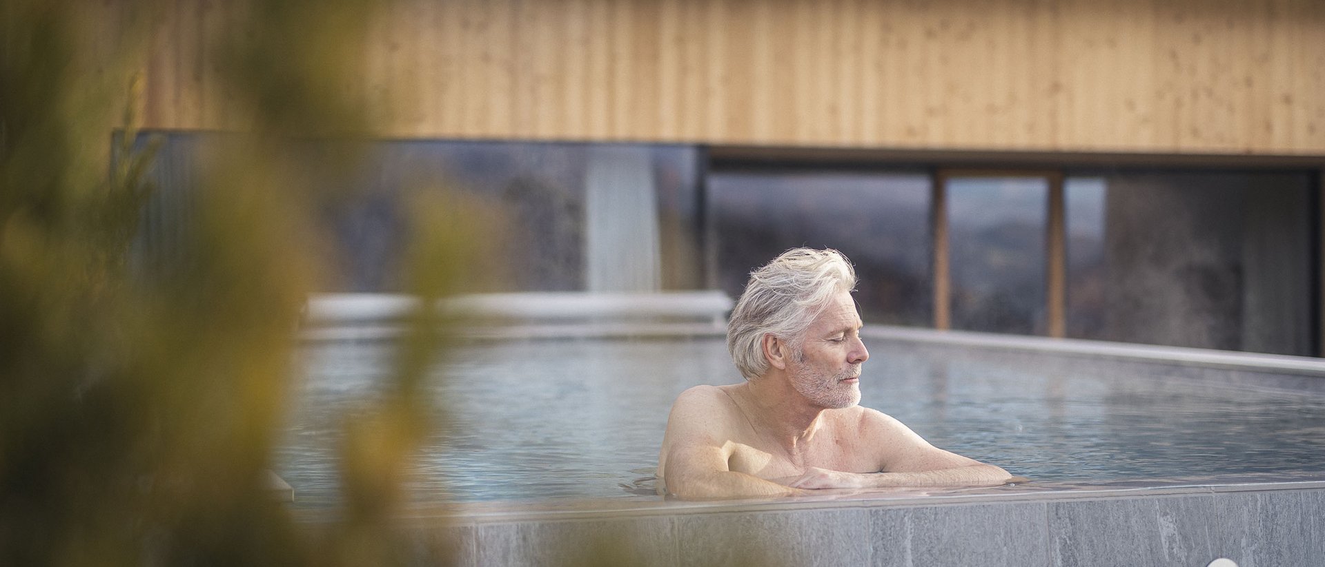 Die Quelle der Erfüllung: Ihr Hotel am Kronplatz Älterer Mann entspannt im Außenpool eines modernen Hauses