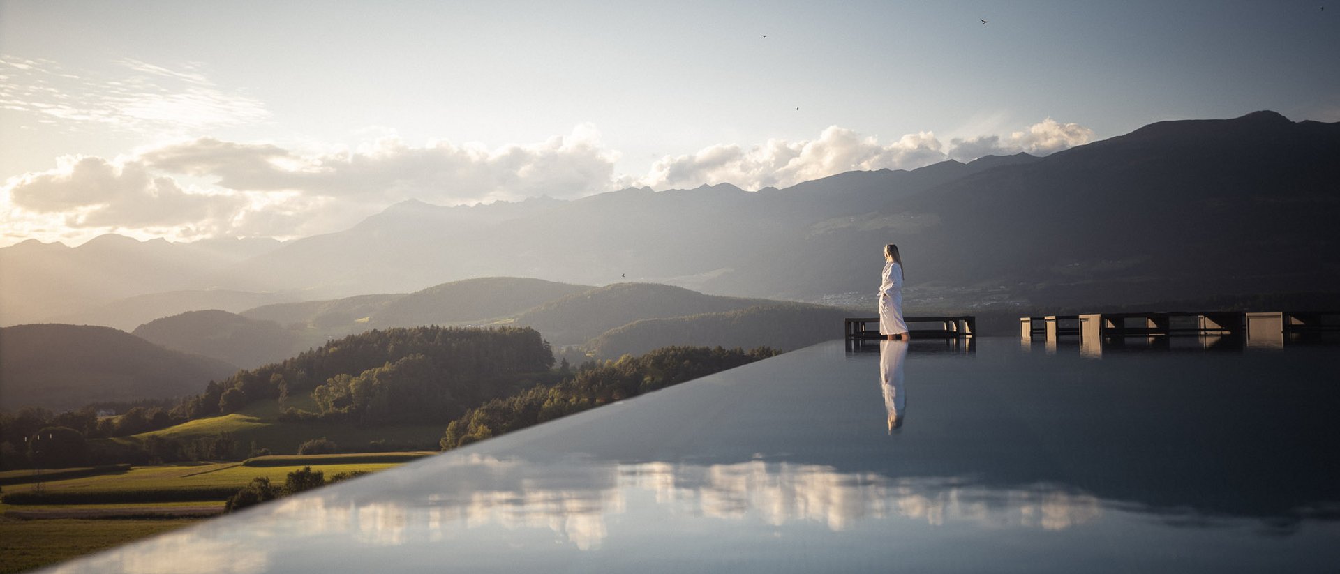 Die Quelle der Erfüllung: Ihr Hotel am Kronplatz Frau steht auf Terrasse mit Bergblick bei Sonnenuntergang