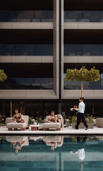 Your hotels in South Tyrol: the home of abundance Two people relaxing on poolside loungers, waitress serving drinks