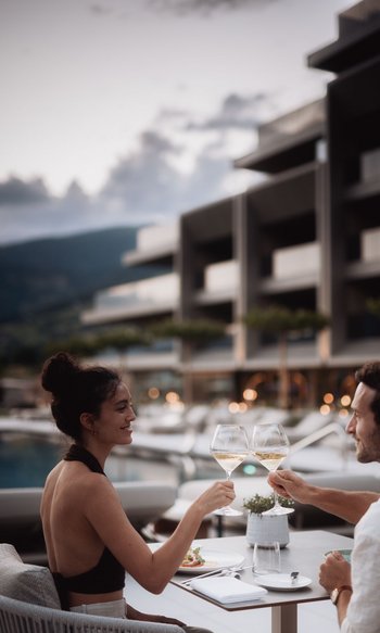 Your hotels in South Tyrol: the home of abundance Couple toasting with white wine on terrace at sunset.