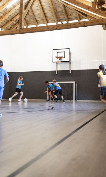 Ihre Hotels in Südtirol: die Heimat der Fülle Kinder spielen Hallenfußball unter Dachbalken auf einem Spielfeld