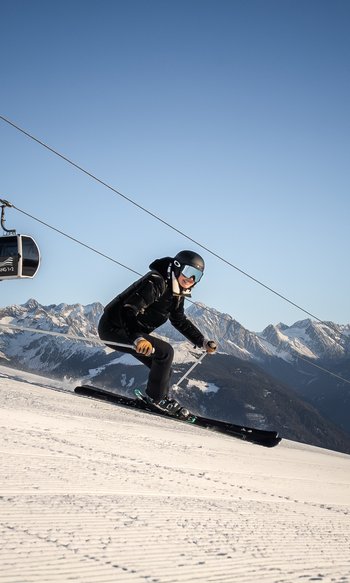 Ihre Hotels in Südtirol: die Heimat der Fülle Skifahrer fährt eine Piste mit Seilbahn und verschneiten Bergen im Hintergrund