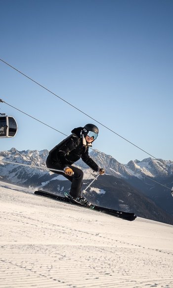 Ihre Hotels in Südtirol: die Heimat der Fülle Skifahrer fährt eine Piste mit Seilbahn und verschneiten Bergen im Hintergrund