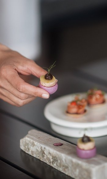Ihre Hotels in Südtirol: die Heimat der Fülle Hand hält ein kleines, farbenfrohes Gourmet-Häppchen an einem gedeckten Tisch