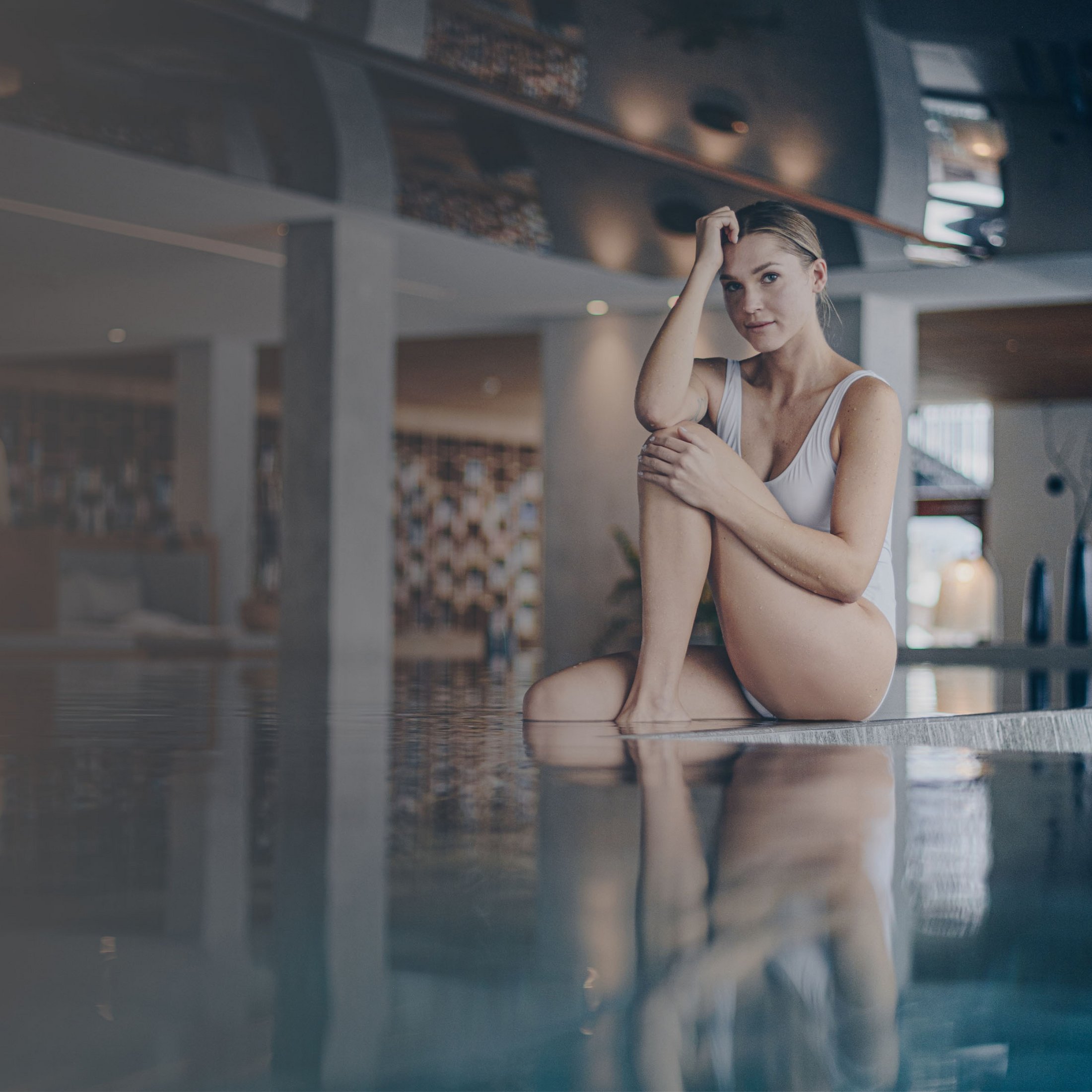 Ihre Hotels in Südtirol: die Heimat der Fülle Frau im weißen Badeanzug sitzt am Rand eines Pools in modernem Innenbereich