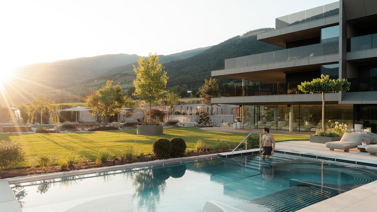 Ihre Hotels in Südtirol: die Heimat der Fülle Mann geht in Pool neben modernem Haus bei Sonnenuntergang in Berglandschaft