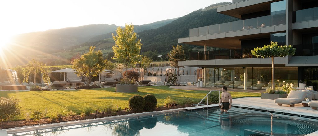 Ihre Hotels in Südtirol: die Heimat der Fülle Mann geht in Pool neben modernem Haus bei Sonnenuntergang in Berglandschaft