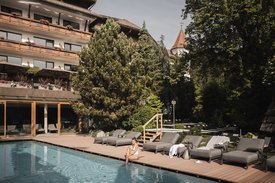 Ihre Hotels in Südtirol: die Heimat der Fülle Frau sitzt am Pool vor Hotel mit Liegestühlen und Bäumen