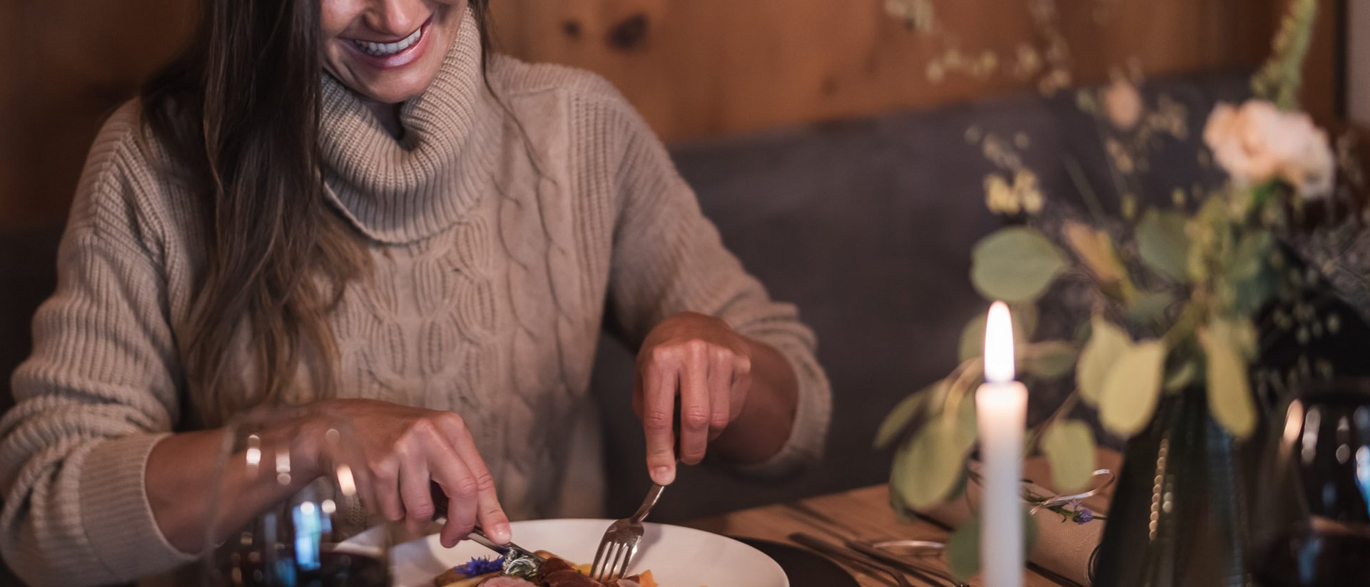 Der Ursprung des Wohlgefühls: Ihr Hotel im Pustertal Frau in beigem Pullover isst ein Gericht in gemütlichem Restaurant