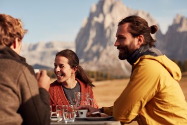 Ihre Hotels in Südtirol: die Heimat der Fülle Drei Freunde genießen Kaffee und Kuchen mit Bergpanorama im Hintergrund