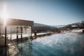 Ihre Hotels in Südtirol: die Heimat der Fülle Dampfender Außenpool mit Bergblick bei klarem Himmel und Sonnenlicht
