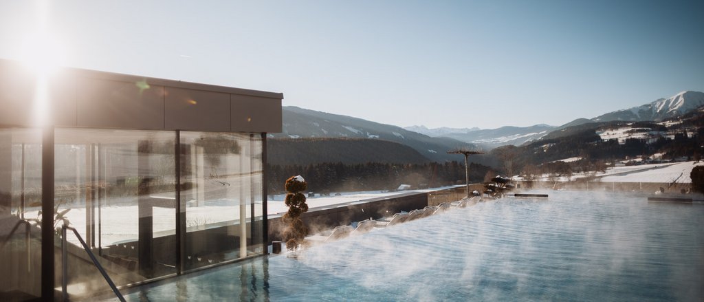 Ihre Hotels in Südtirol: die Heimat der Fülle Dampfender Außenpool mit Bergblick bei klarem Himmel und Sonnenlicht