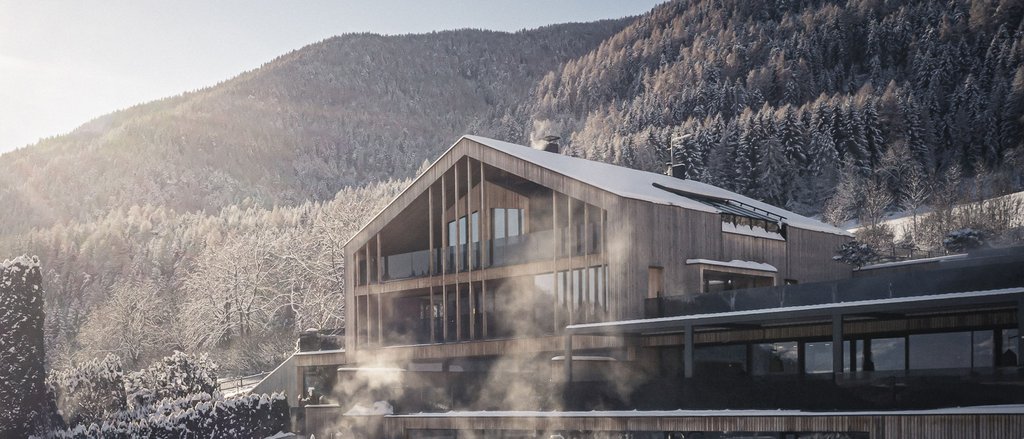 Ihre Hotels in Südtirol: die Heimat der Fülle Modernes Holzhaus mit Schnee und Nebel vor bewaldetem Berg
