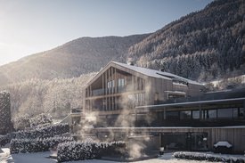 Ihre Hotels in Südtirol: die Heimat der Fülle Modernes Holzhaus mit Schnee und Nebel vor bewaldetem Berg