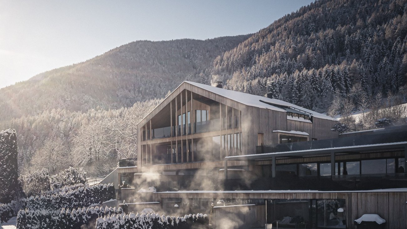 Ihre Hotels in Südtirol: die Heimat der Fülle Modernes Holzhaus mit Schnee und Nebel vor bewaldetem Berg